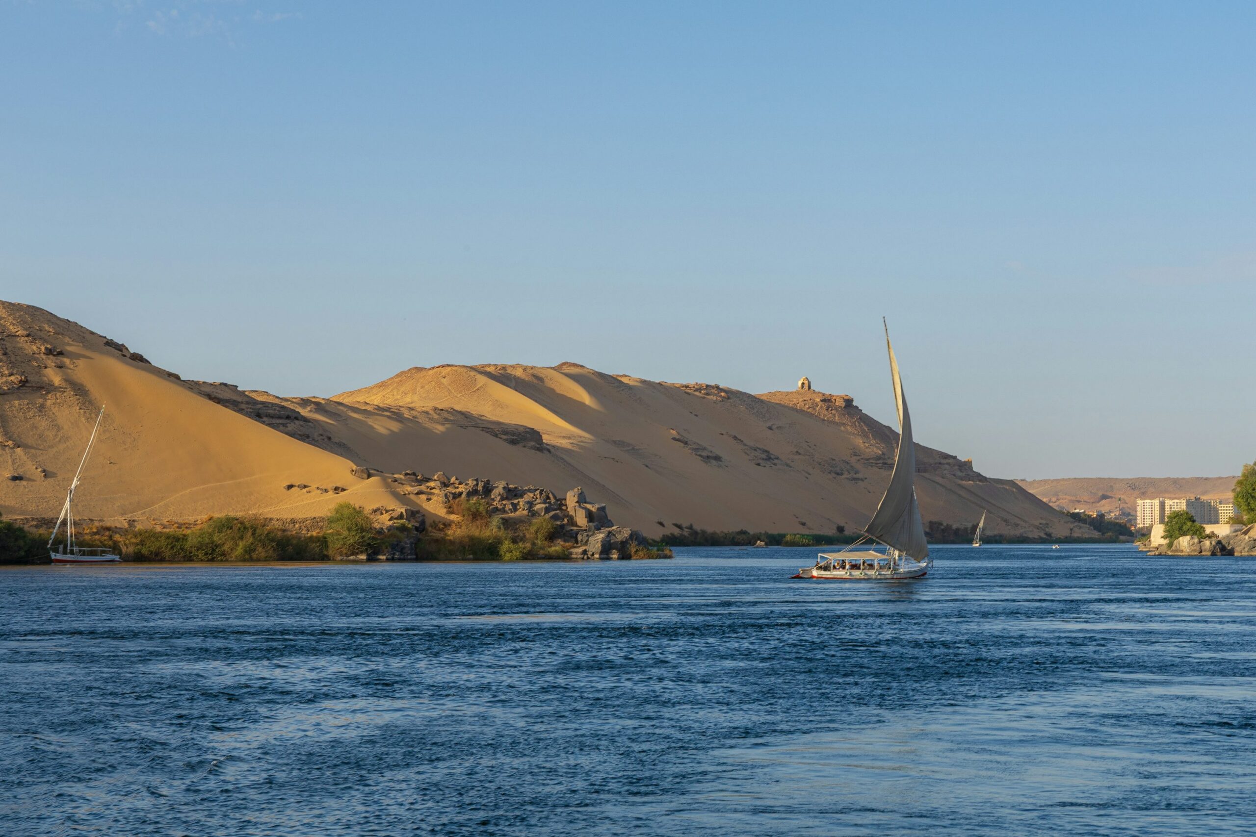 Sailboats on the Nile River with greenery and desert hills in daylight